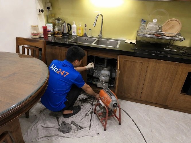 Thợ alo247 đang thông tắc bồn rửa bát bằng máy lò xo chuyên dụng