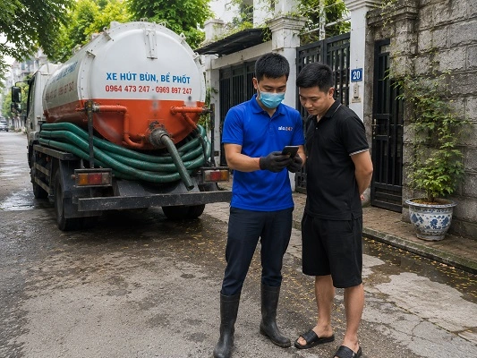 Thợ giải thích phương án hút bể phốt bằng xe chân không cho khách hàng tại Đông Anh