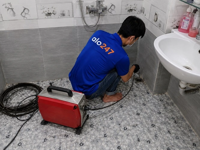 Thợ alo247 đang sử dụng máy lò xo để thông tắc cống sàn nhà vệ sinh tại Cầu Giấy