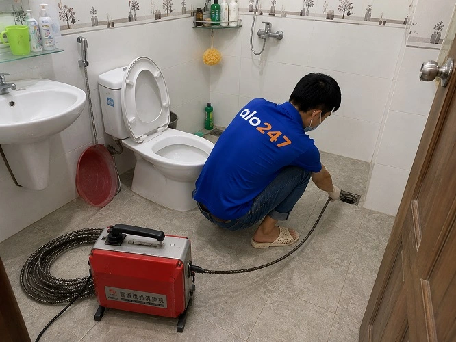 Thợ alo247 đang sử dụng máy lò xo để thông tắc cống sàn nhà vệ sinh tại Hoàng Mai