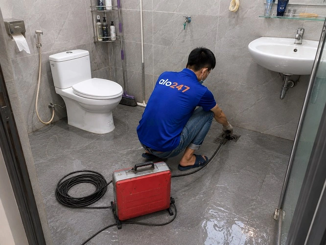 Thợ alo247 đang sử dụng máy lò xo để thông tắc cống sàn nhà vệ sinh tại Thanh Trì