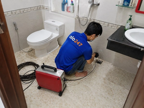 Thợ alo247 đang sử dụng máy lò xo để thông tắc cống sàn nhà vệ sinh tại Thanh Xuân