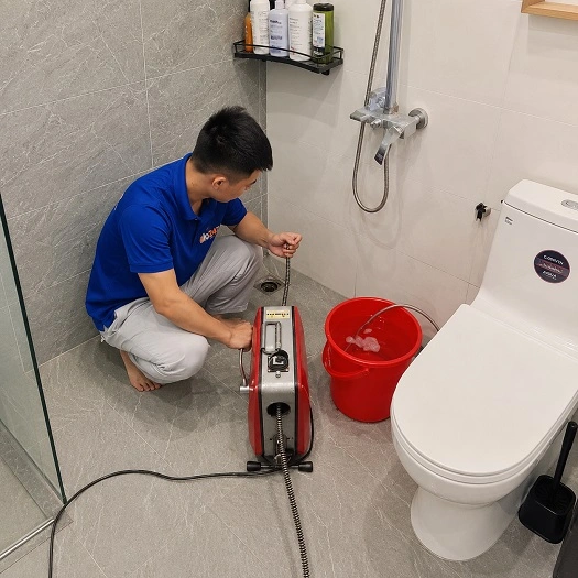 Thợ alo247 đang sử dụng máy lò xo để thông tắc cống sàn nhà vệ sinh tại Bạch Mai