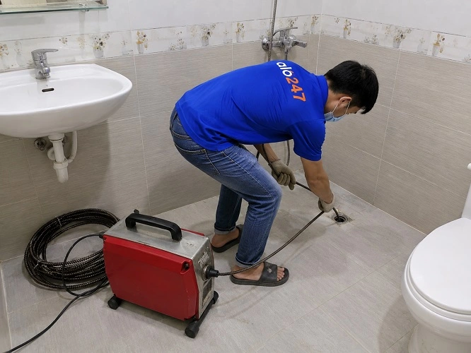 Thợ alo247 đang sử dụng máy lò xo để thông tắc cống sàn nhà vệ sinh tại Khương Đình