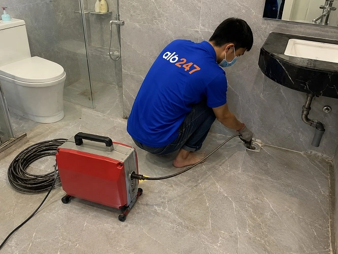 Thợ alo247 đang sử dụng máy lò xo để thông tắc cống sàn nhà vệ sinh tại Láng