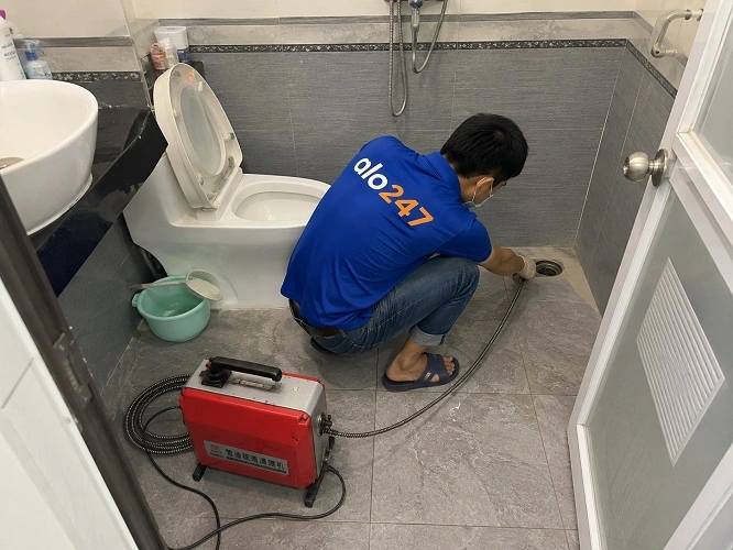 Thợ alo247 đang sử dụng máy lò xo để thông tắc cống sàn nhà vệ sinh tại Lĩnh Nam