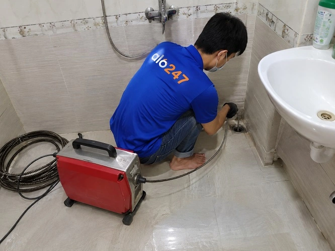 Thợ alo247 đang sử dụng máy lò xo để thông tắc cống sàn nhà vệ sinh tại Ô chợ Dừa