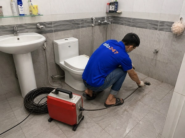 Thợ alo247 đang sử dụng máy lò xo để thông tắc cống sàn nhà vệ sinh tại Phú Thượng
