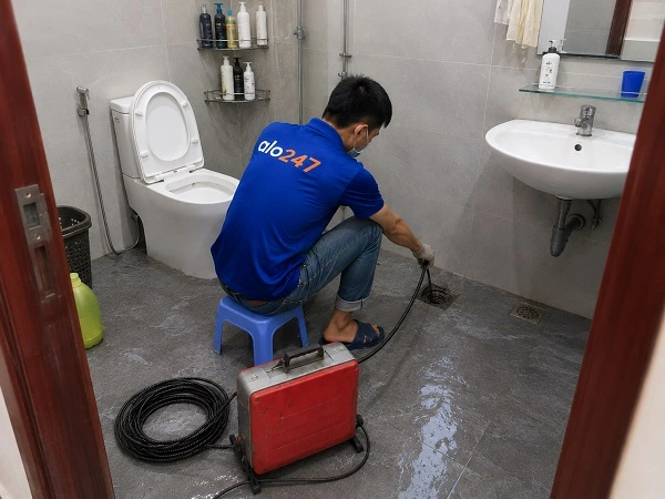 Thợ alo247 đang sử dụng máy lò xo để thông tắc cống sàn nhà vệ sinh tại Việt Hưng