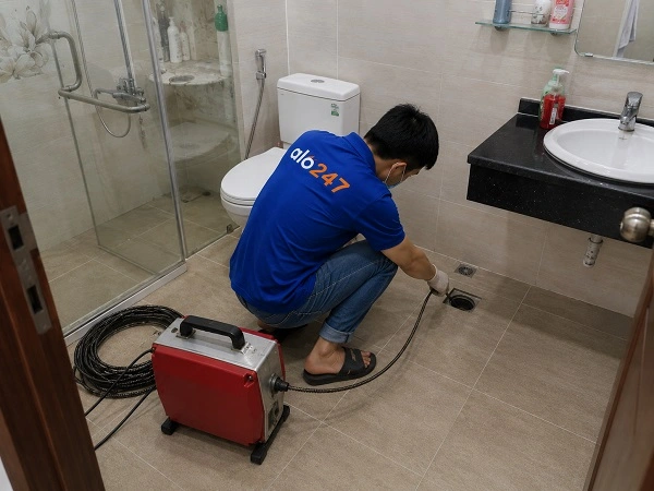 Thợ alo247 đang sử dụng máy lò xo để thông tắc cống sàn nhà vệ sinh tại Yên Sở