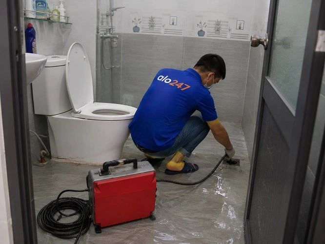 Thợ alo247 đang sử dụng máy lò xo để thông tắc cống sàn nhà vệ sinh tại Thanh Liệt